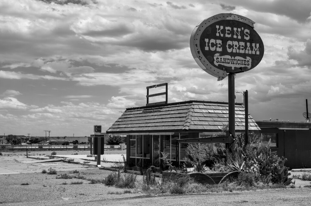 Black and white image of an abandoned ice cream stand with vintage signage and a desolate atmosphere.